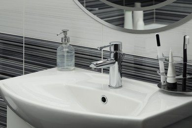 Clean white sink with shiny water tap and toiletries in bathroom