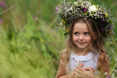 Cute little girl wearing wreath made of beautiful flowers in field