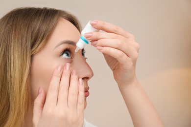 Young woman using eye drops on beige background