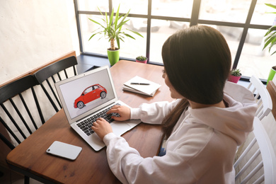 Photo of Woman using laptop to buy car at wooden table indoors
