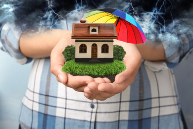 Insurance concept - umbrella demonstrating protection. Woman holding house model with green lawn, closeup