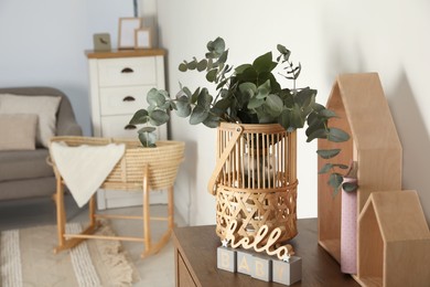 Wicker basket with beautiful eucalyptus branches and phrase Hello Baby on wooden table indoors, space for text. Interior design