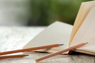 Closeup view of open notebook with pencils on white wooden table against blurred background