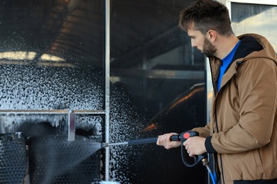 Man cleaning auto mats with high pressure water jet at self-service car wash
