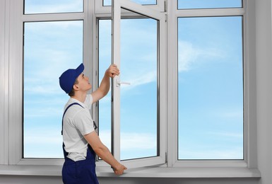 Worker in uniform installing plastic window indoors