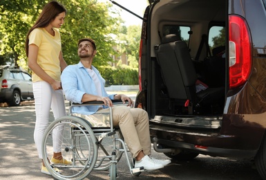 Young woman helping man in wheelchair to get into van outdoors