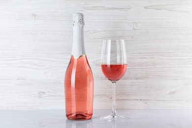 Bottle and glass of delicious rose wine on table against white wooden background