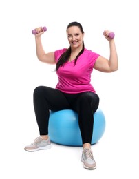 Happy overweight woman with dumbbells sitting on fitness ball against white background