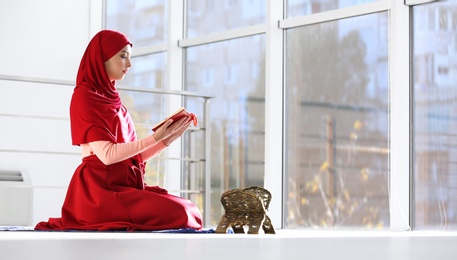Muslim woman in hijab reading Koran indoors. Space for text