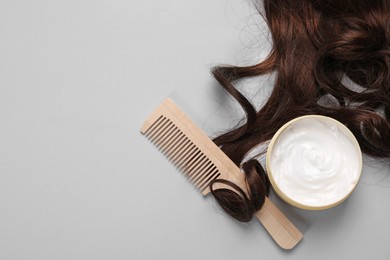 Lock of healthy brown hair, comb and cosmetic product on light grey background, flat lay. Space for text