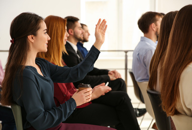 Young woman raising hand to ask question at business training indoors