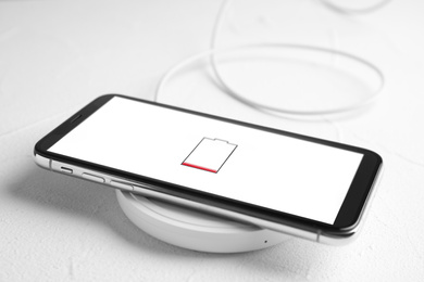 Mobile phone charging with wireless pad on white stone table, closeup