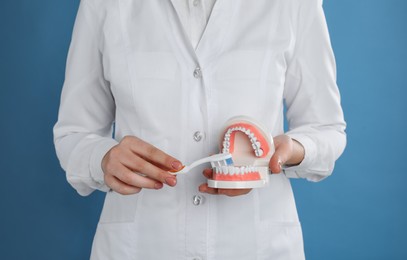 Dentist with jaws model and toothbrush on light blue background, closeup. Oral care demonstration
