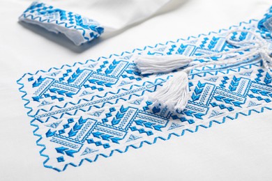 Photo of Beautiful white shirt with light blue Ukrainian national embroidery, closeup