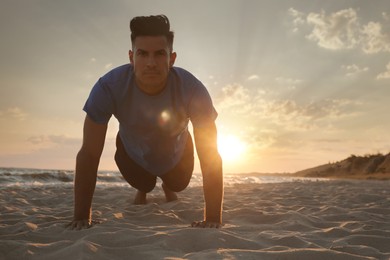 Sporty man doing plank on sandy beach at sunset