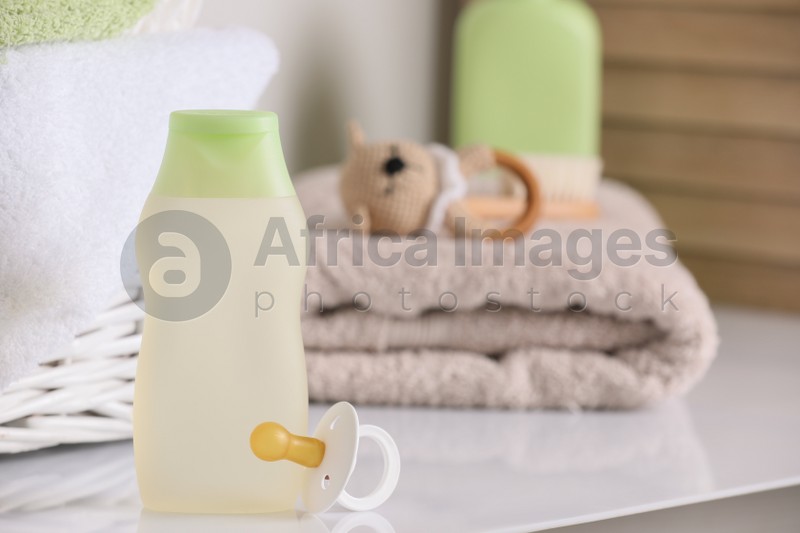 Photo of Bottle of baby cosmetic product and pacifier near accessories on white table. Space for text