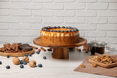Photo of Delicious cheesecake with caramel and blueberries on white wooden table near brick wall