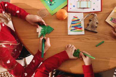 Little children making Christmas crafts at wooden table, top view