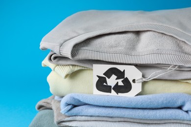 Stack of clothes with recycling label on light blue background, closeup