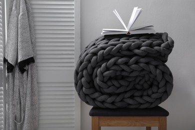 Dark grey chunky knit blanket rolled on wooden stool in room