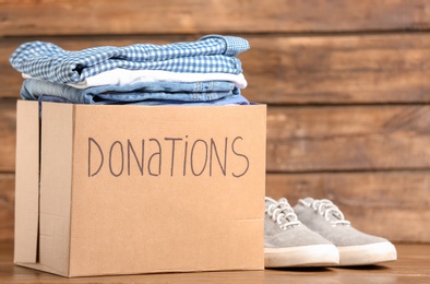 Photo of Donation box with clothes on wooden background