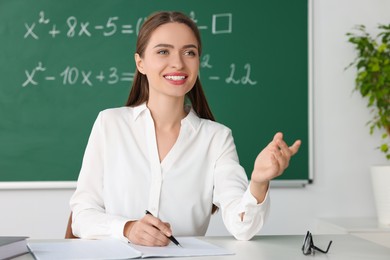 Photo of Young math’s teacher giving lesson at table in classroom