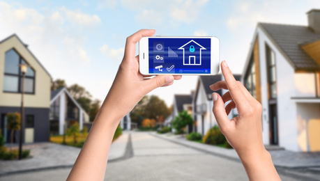 Image of Woman using home security app on smartphone outdoors, closeup