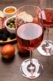 Delicious rose wine and snacks on wooden table, closeup