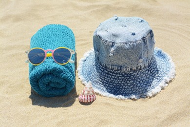 Towel with sunglasses, seashell and denim hat on sand outdoors. Beach accessories
