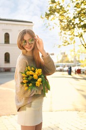 Beautiful teenage girl with bouquet of yellow tulips on city street