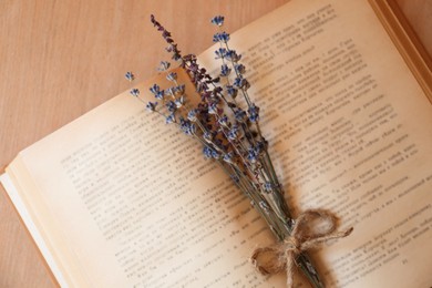 Open book with bunch of dried flowers on wooden table, closeup