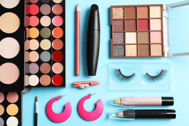 Set of makeup products and earrings on light blue background, flat lay