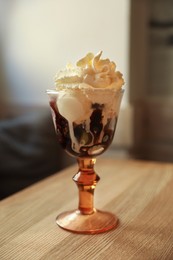Photo of Delicious dessert with whipped cream in glass on wooden table indoors