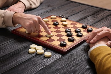Photo of Man playing checkers with partner at black wooden table indoors, closeup