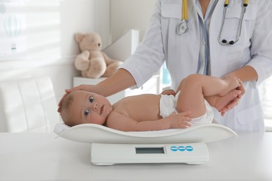 Pediatrician weighting cute baby in clinic, closeup. Health care
