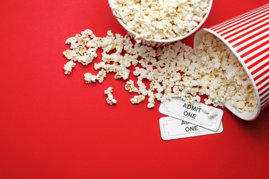 Popcorn and tickets on red background, flat lay. Cinema snack