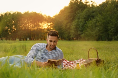 Young man reading book on picnic blanket in park