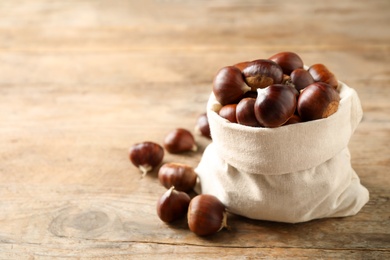 Fresh sweet edible chestnuts in sack on wooden table. Space for text