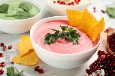Bowl of delicious pink hummus with tortilla chips and parsley on white marble table