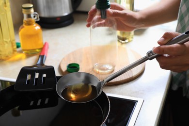 Woman with used cooking oil and empty bottle near stove in kitchen, closeup