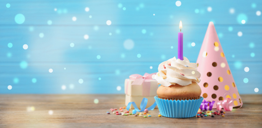 Composition with birthday cupcake on wooden table, space for text. Bokeh effect