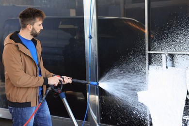 Man cleaning auto mats with high pressure foam jet at self-service car wash