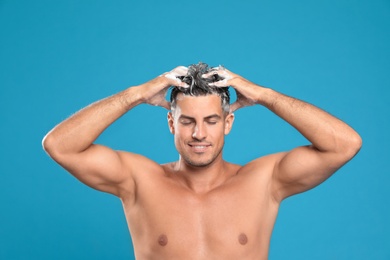 Handsome man washing hair on light blue background