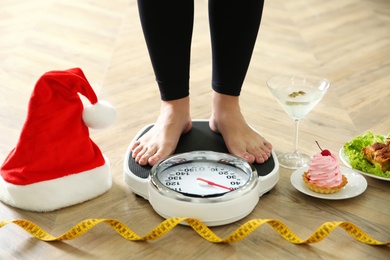 Food, alcohol left after Christmas holidays and woman with measuring tape standing on scales indoors, closeup. Overweight problem