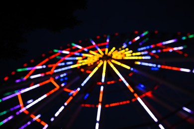 Blurred view of beautiful glowing Ferris wheel against dark sky
