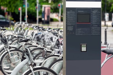 Photo of Payment terminal near parking lot with many bicycles outdoors. Bike rental