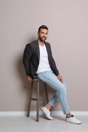 Handsome man sitting on stool near beige wall