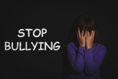 Message STOP BULLYING and abused little girl crying near black wall