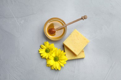 Natural beeswax, honey and flowers on light grey stone table, flat lay