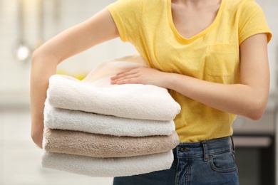 Woman holding folded clean towels in kitchen, closeup. Laundry day